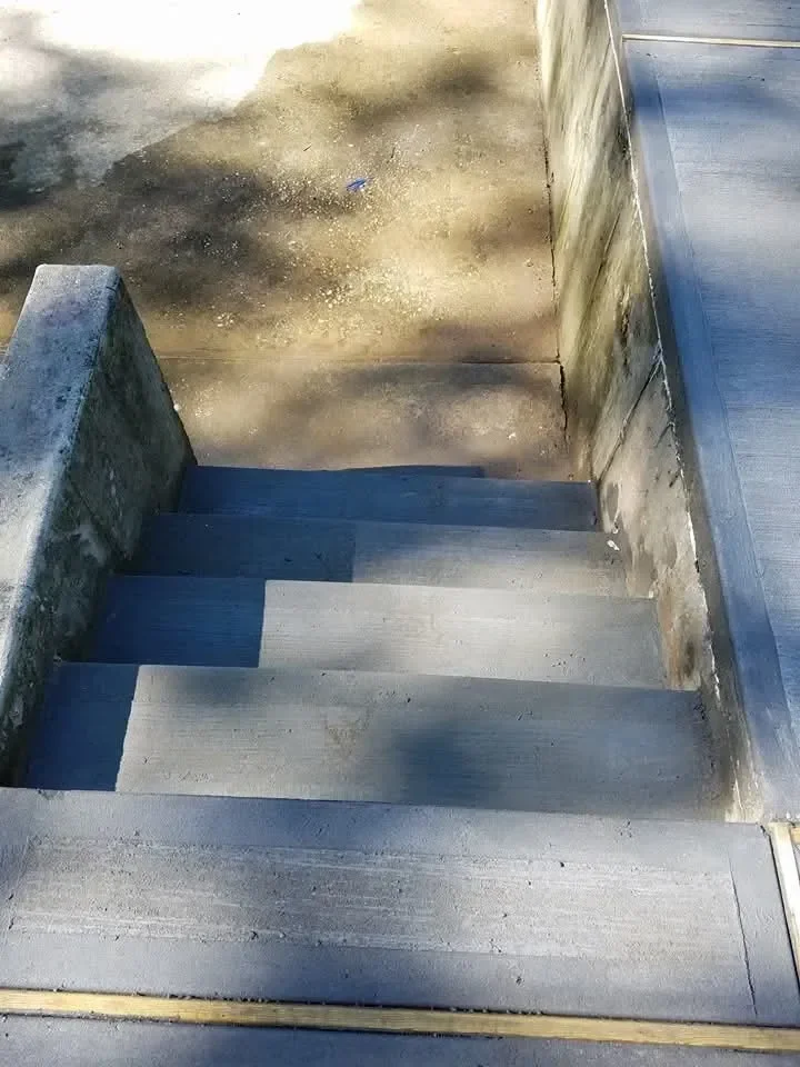 A view looking down a set of gray concrete stairs bordered by concrete walls, contrasting sharply with the dirty, stained landing area above.