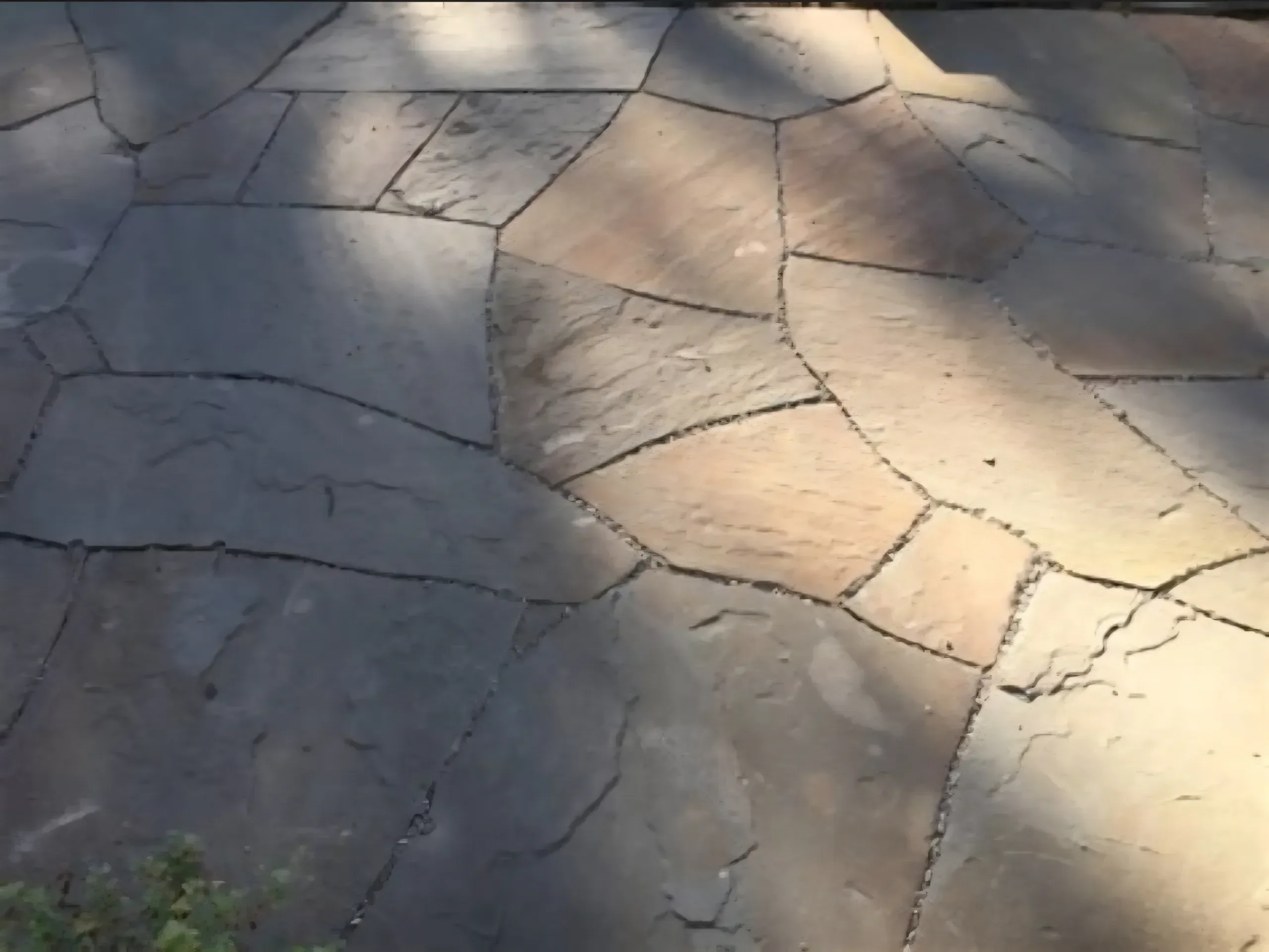 A close-up view of completed irregular natural stone flagstone paving, showing variations in color and texture under dappled sunlight.