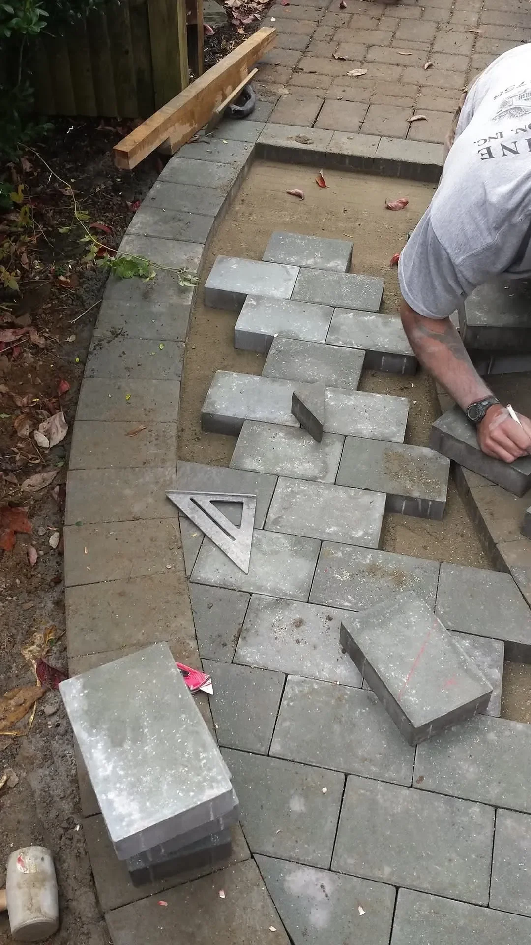A hardscaper squares gray pavers along a newly built curved patio edge.