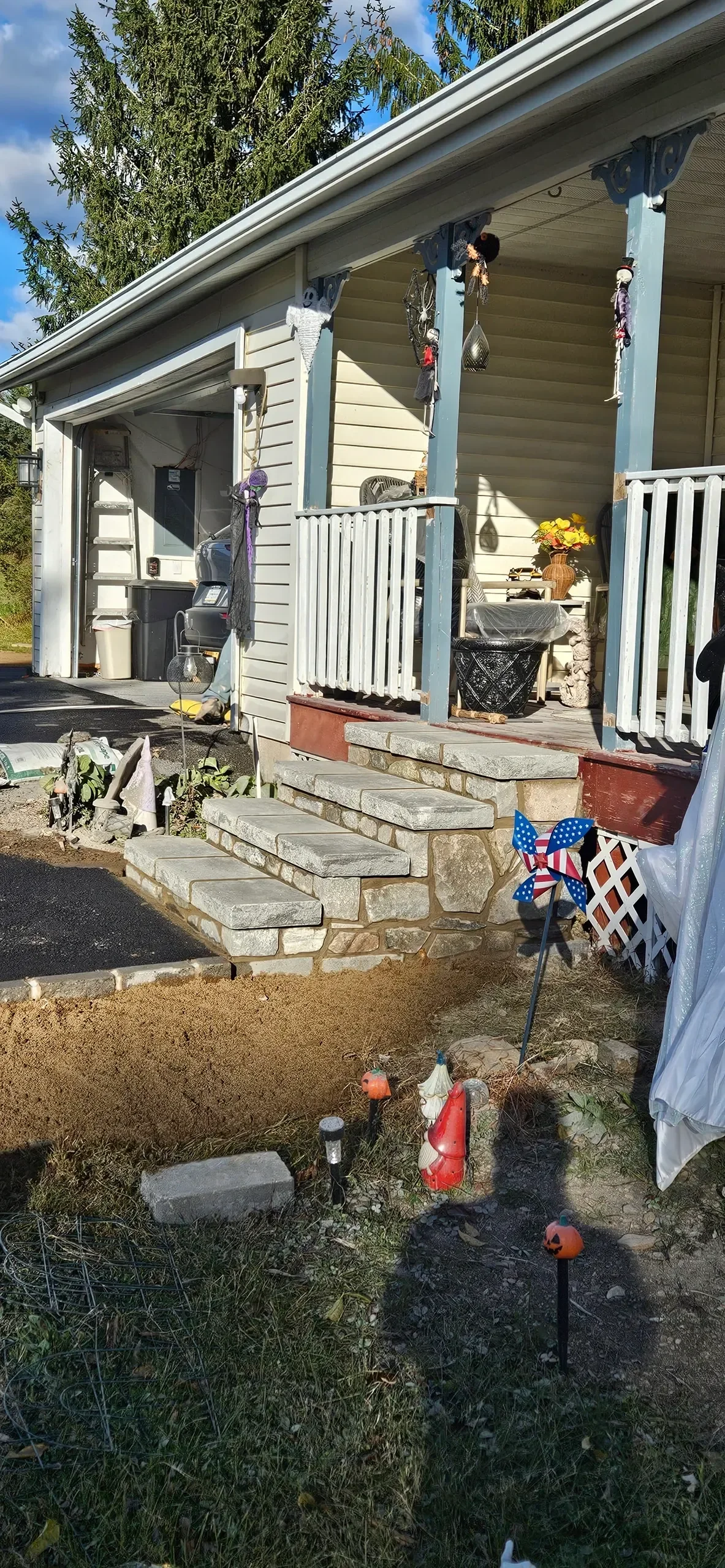 Newly constructed stone steps lead up to a residential porch decorated for Halloween, with evidence of ongoing hardscaping work visible in the foreground.
