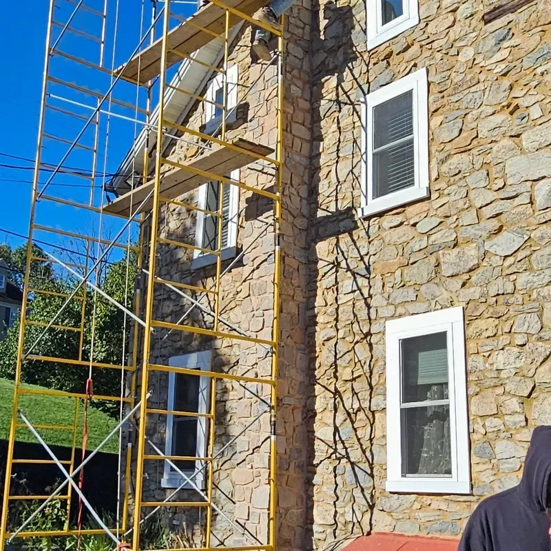 Yellow scaffolding is set up against the rough-cut stone exterior of a building where renovation work is actively taking place under a blue sky.